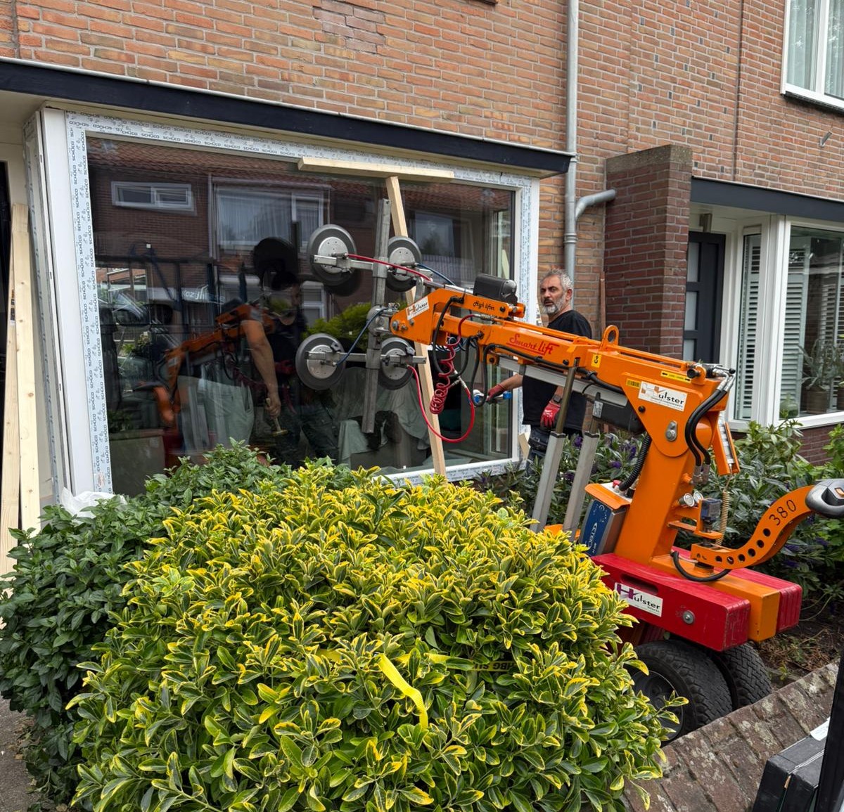 Plaatsen van een groot HR++ raam in een bakstenen gevel met behulp van een glaslift tijdens een woningrenovatie.