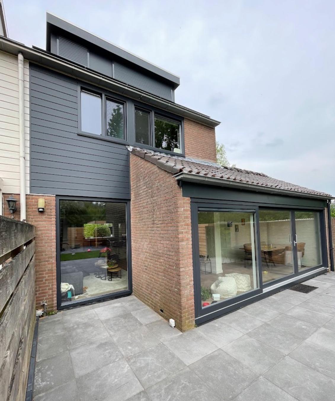 Donkergrijze kunststof gevelbekleding op woning met moderne kozijnen en aanbouw