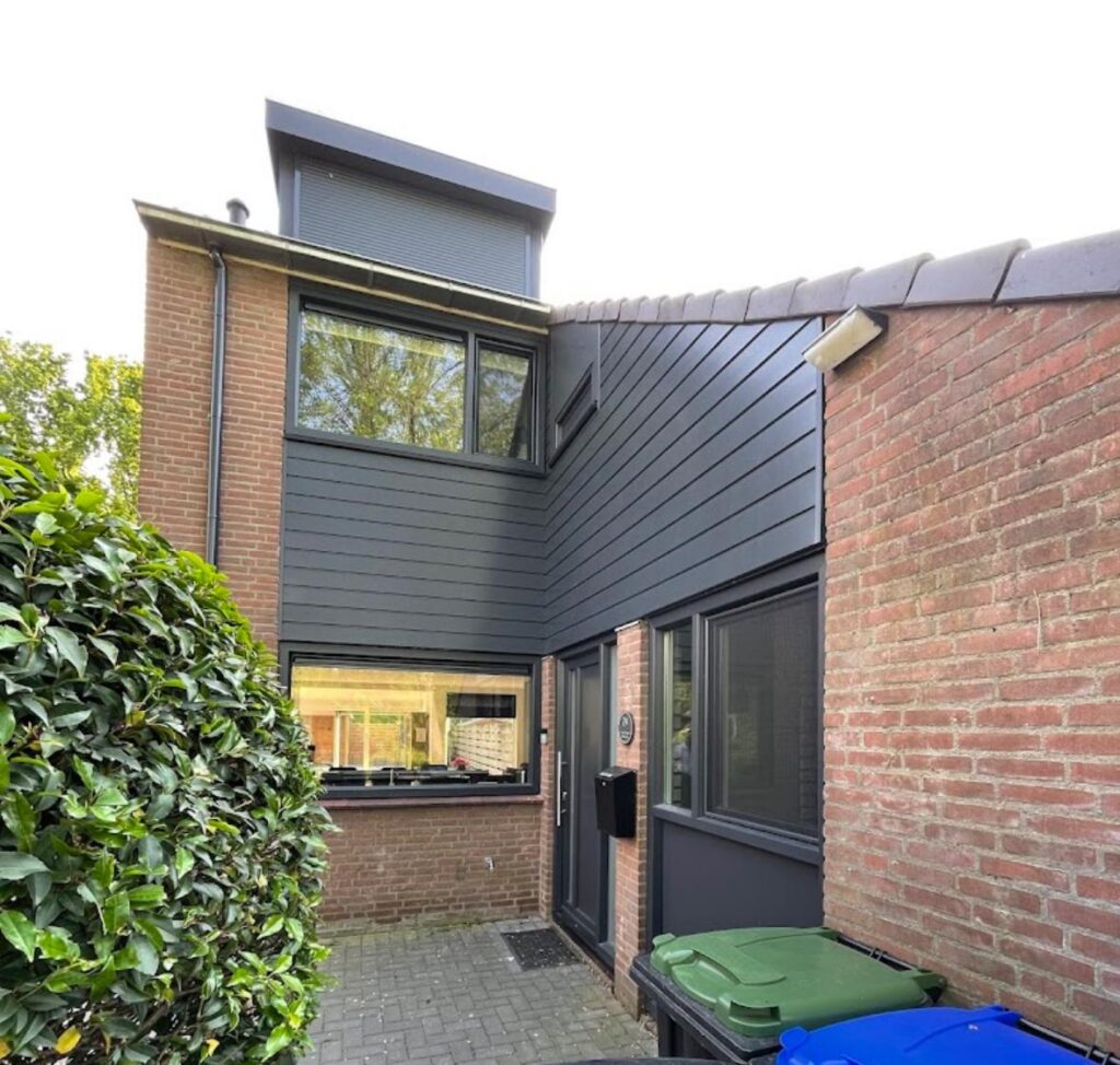 Donkergrijze kunststof gevelbekleding op woning met moderne kozijnen en aanbouw